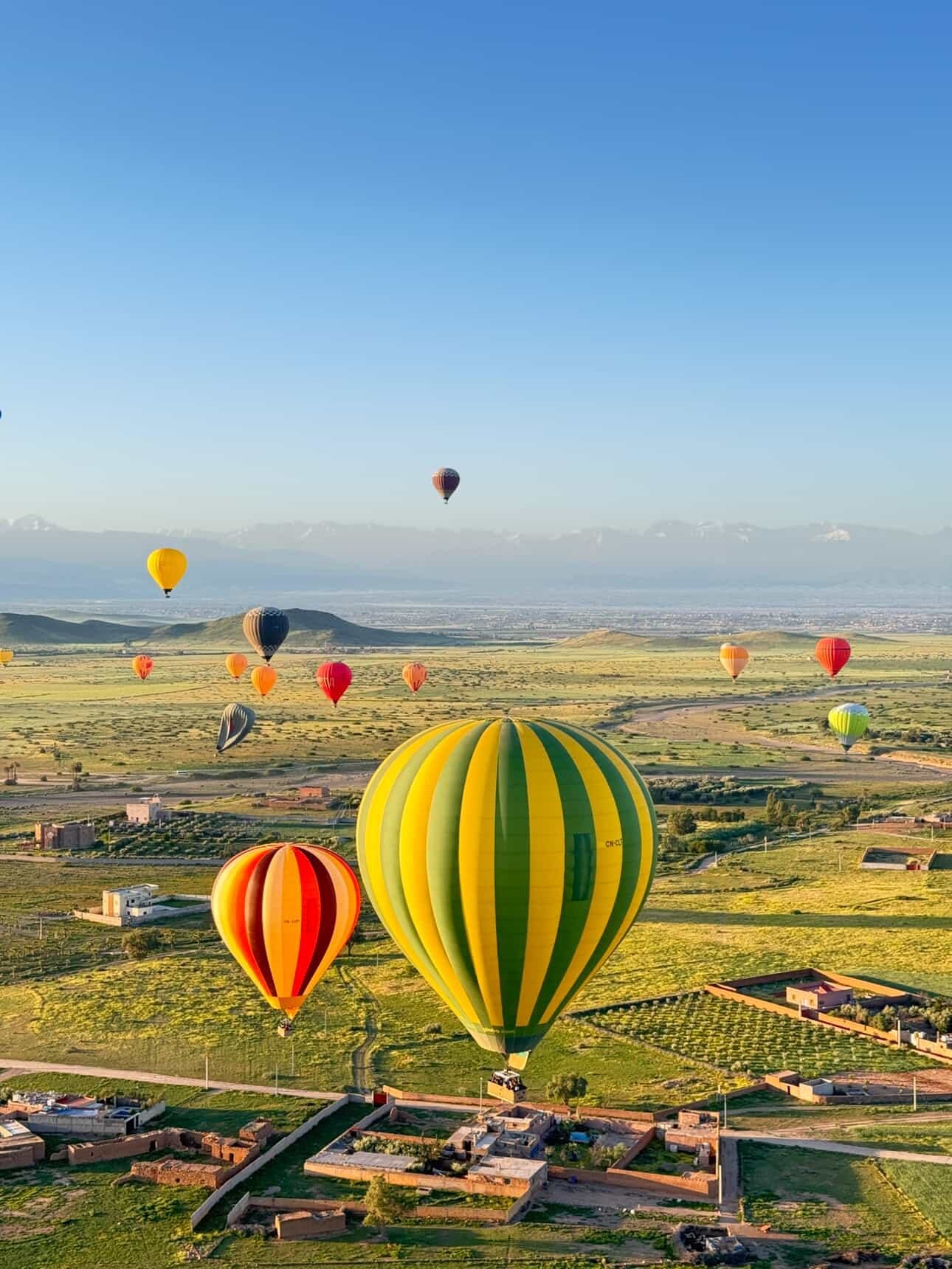 Globos aerostáticos sobre campos verdes y pueblos cerca de Marrakech con el Atlas nevado